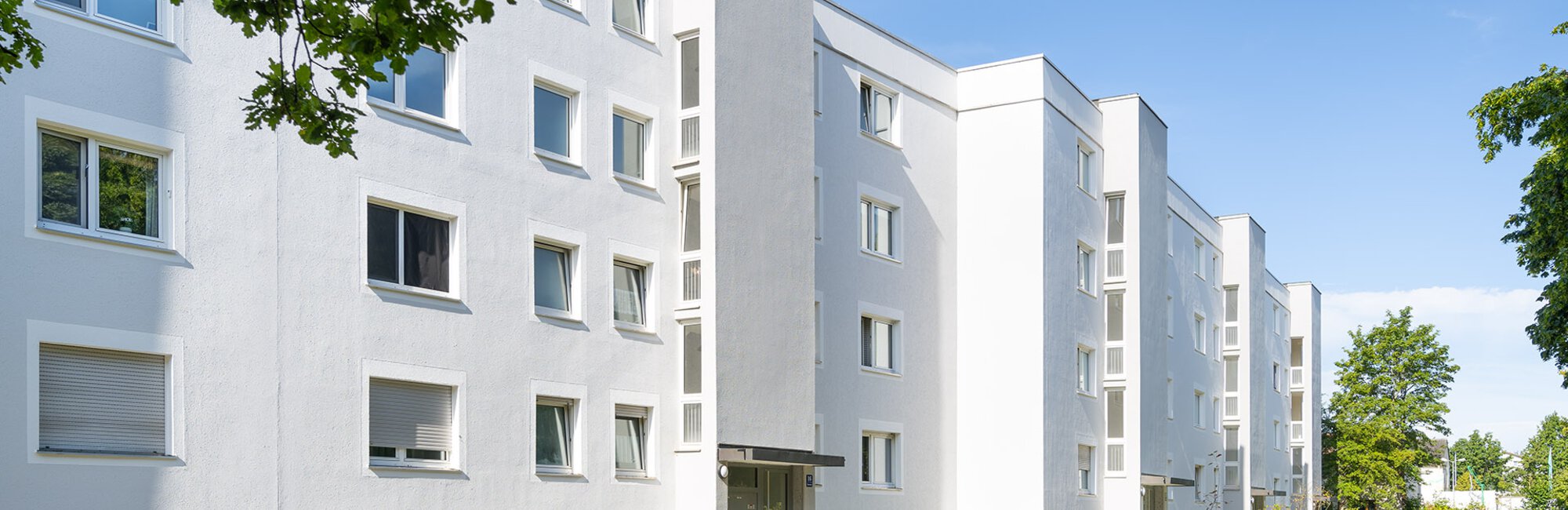 Außenansicht Kaufobjekt in Fürstenfeldbruck. Weiße Fassade mit Außenfahrstühlen direkt neben den Eingängen