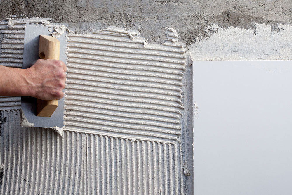 Handwerker trägt Fliesenkleber auf eine Wand auf – symbolisch für praktische Erfahrung im Bauwesen